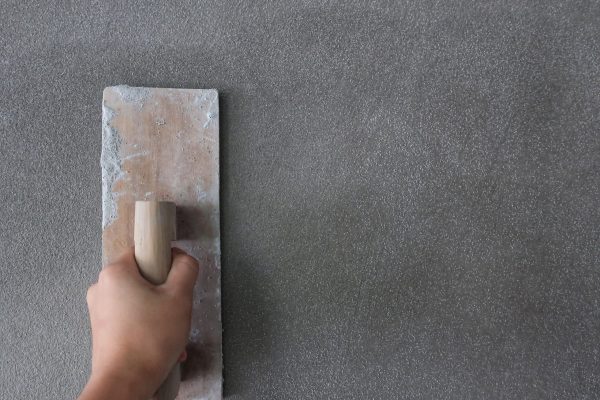 nahaufnahme-eines-arbeiters-der-auf-einer-grauen-wand-auf-einer-baustelle-mit-einem-schaber-arbeitet nahaufnahme-eines-arbeiters-der-auf-einer-grauen-wand-auf-einer-baustelle-mit-einem-schaber-arbeitet